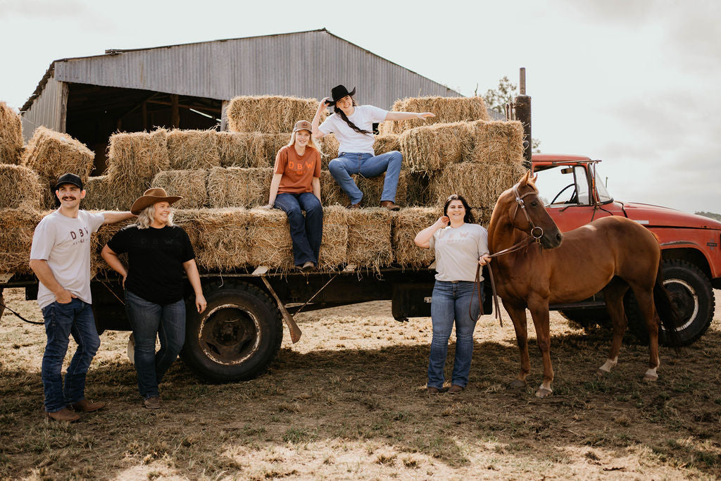 Group of people posing on a truck loaded with hay bales, with a horse nearby in a rural farm setting